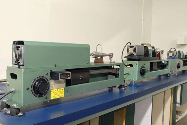 Three green-painted rotating beam fatigue testing equipment units on blue counter