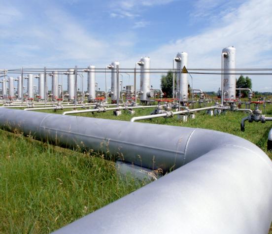 Large natural gas farm transmission pipes in foreground with additional piping and storage pipes in the background