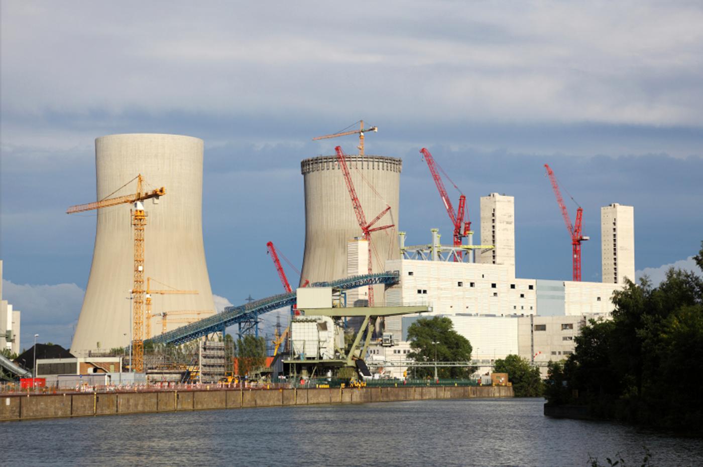 Construction of nuclear power plant cooling towers with water in foreground and cranes used in construction