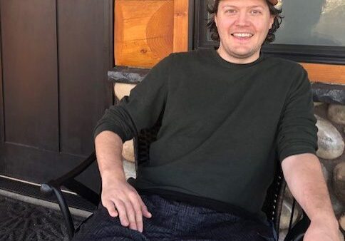 Alex Fish, materials science engineer at IMR Test Labs- Portland, shown relaxing in a rocking chair on a log cabin's front porch