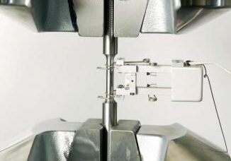 Close-up of tensile testing equipment with metal dog bone sample clamped in and sensor attached