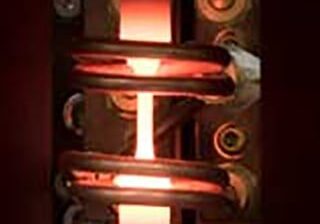 Metal sample glowing red from heat applied by 2 heating elements surrounding the sample during high temperature fatigue testing